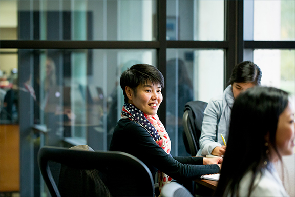 Short black haired person looking forward and smiling during a meeting.