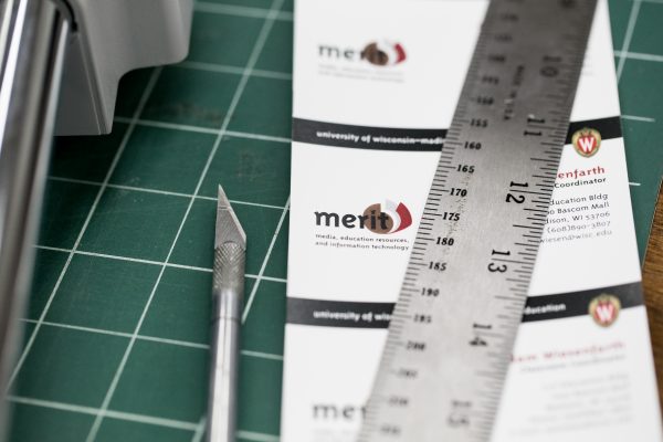 X-Acto knife, metal ruler and MERIT library cards on white and green grid.