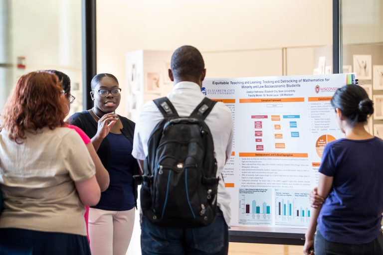 Summer Education Research Program students gather around a tri-fold poster.