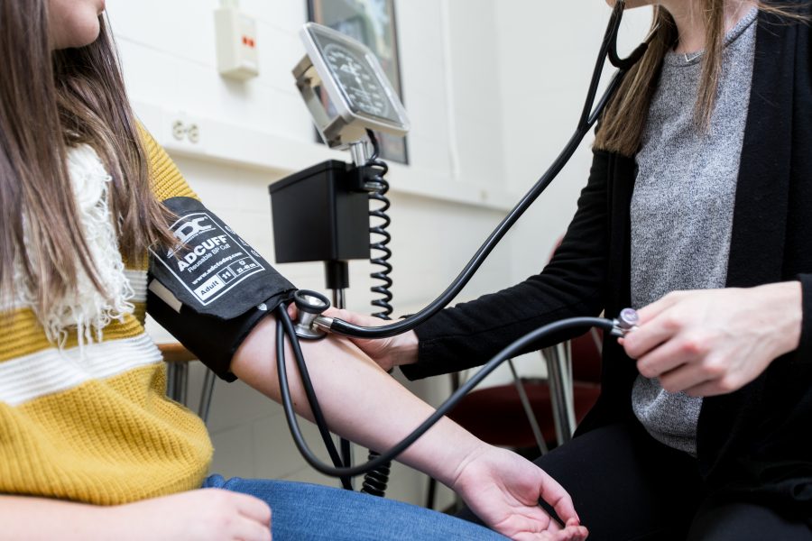 A female student takes the blood pressure of a student in a yellow shirt.