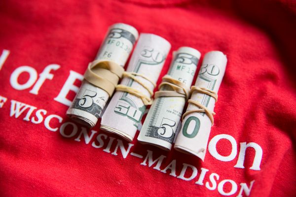 4 rolls of $50 atop of red UW-Madison School of Education t-shirt.