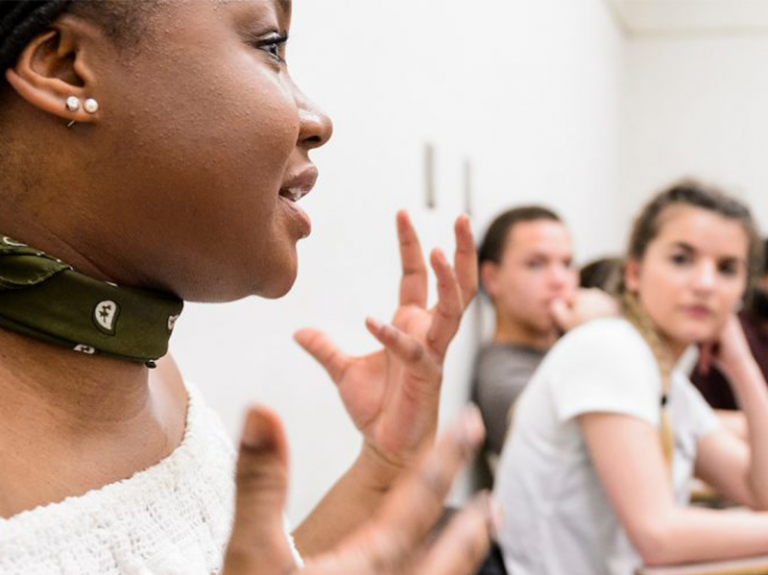 Student gesturing with hands as they speak while other students watch.