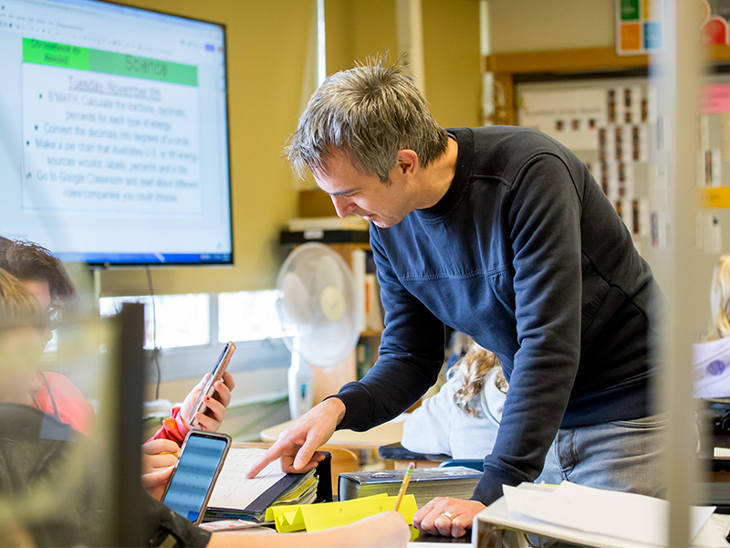 Teacher pointing to paper as students use their phone calculator.