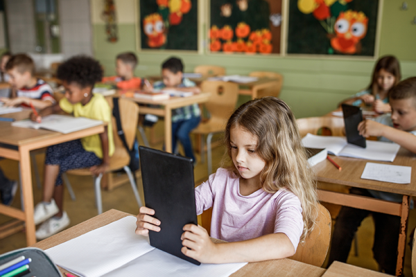 Children holding a black tablet as they draw in a classroom.