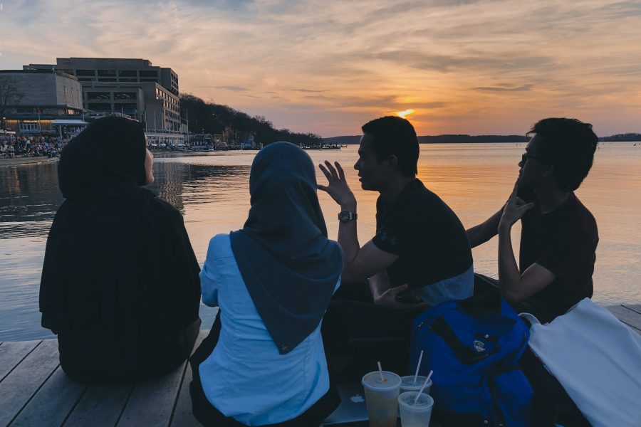 Four individuals sitting on a dock on Lake Mendota during the sunset.